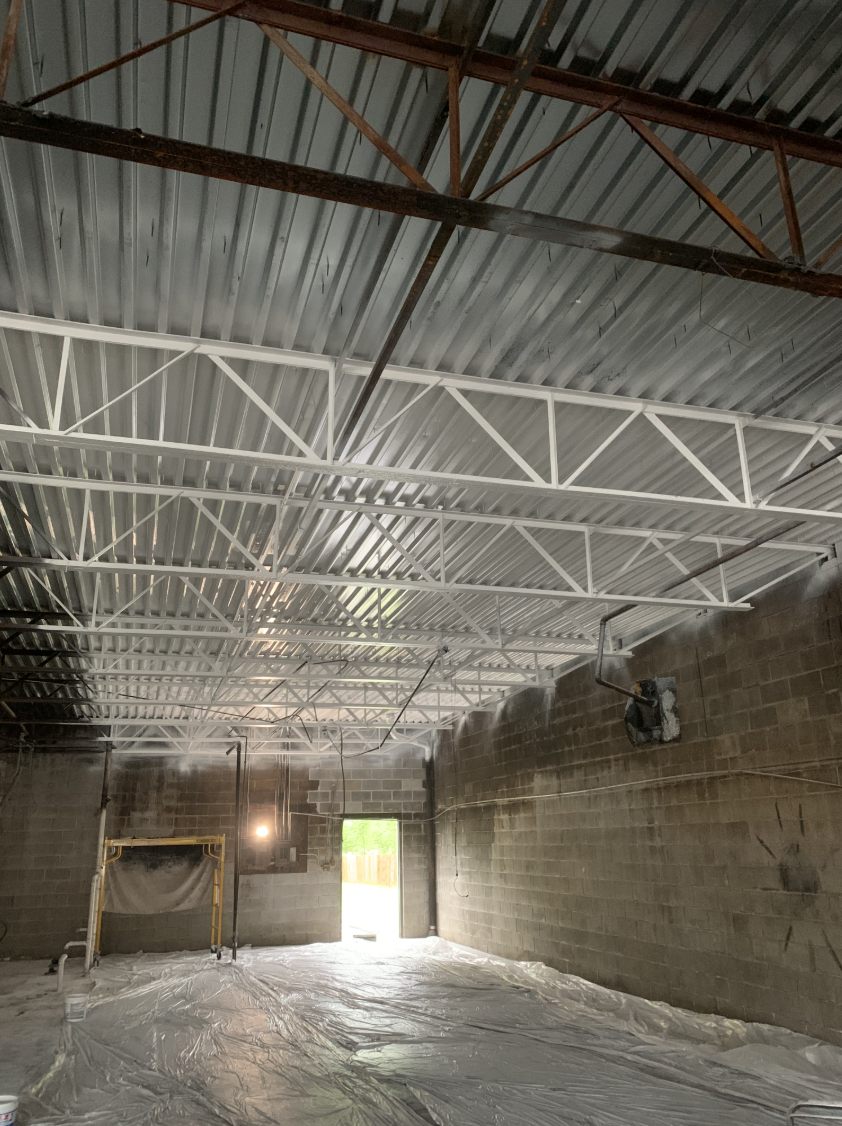 Commercial interior mid-build in Northeast Ohio — exposed steel trusses, freshly painted ceiling, block walls prepped for finish work